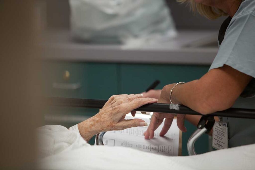 Nurse reviewing a medication list and care plan with an older resident at a dining table.